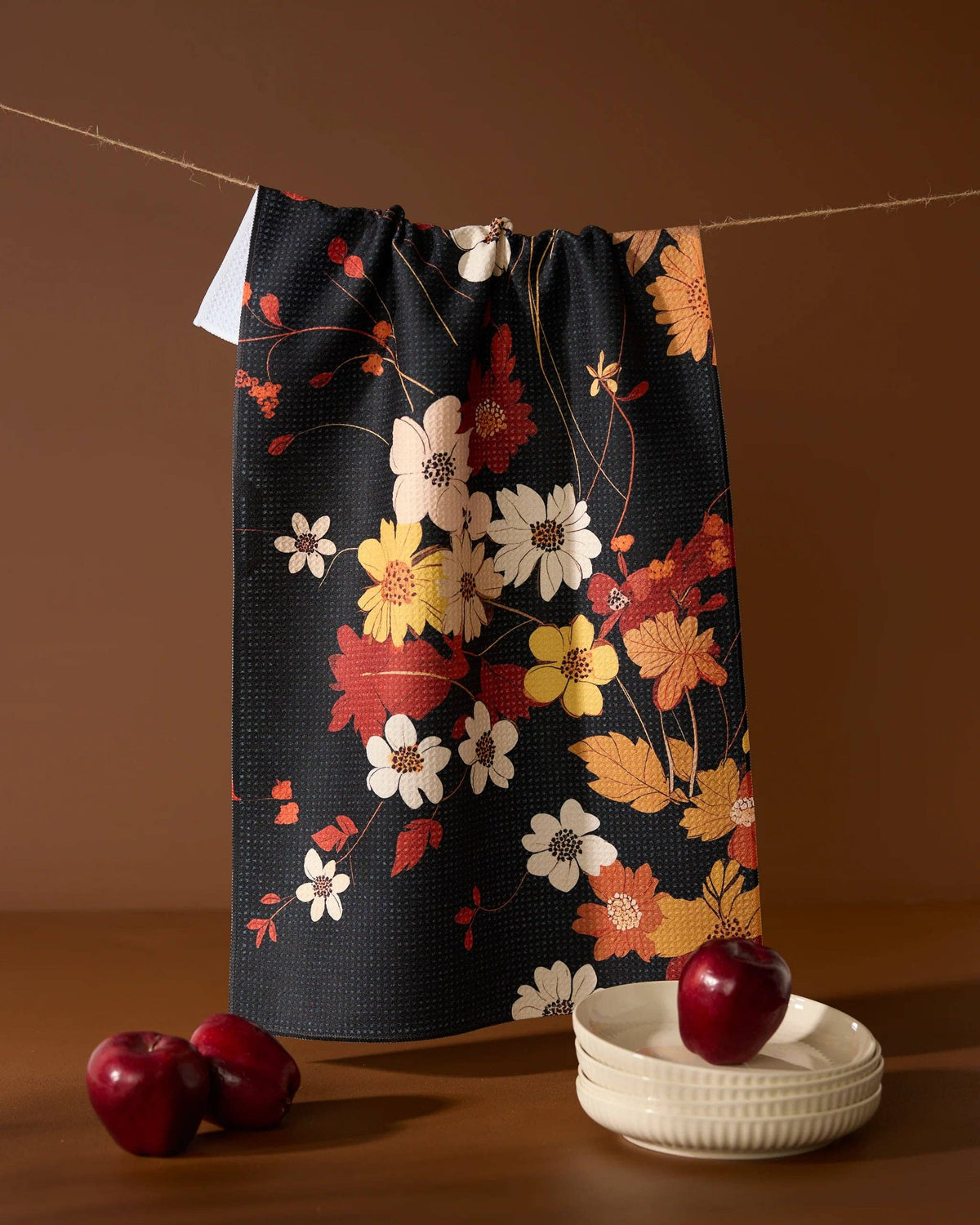 Floral-patterned tea towel on a string with apples and a bowl on a brown background