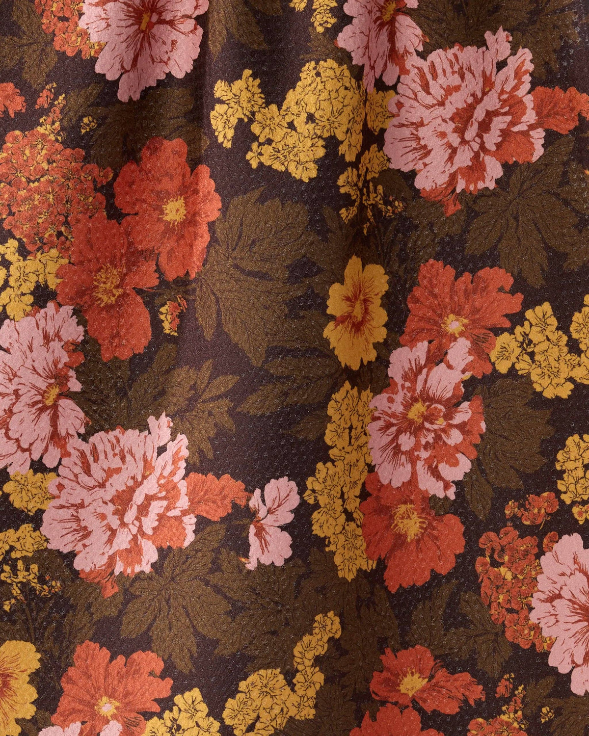 A close-up of a floral fabric pattern featuring large pink and orange flowers with yellow accents on a dark brown background.